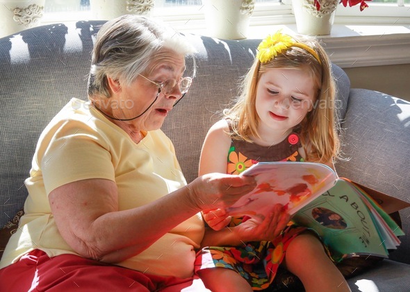 Grandma and granddaughter reading a book together on the couch