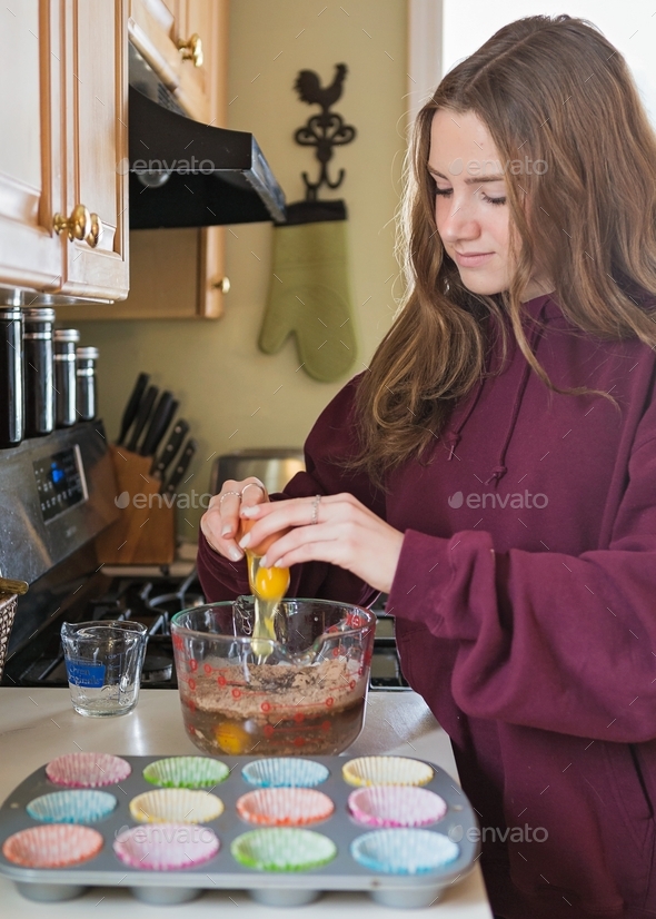 Teenage girl cracking an egg into cake batter mix to bake cupcakes