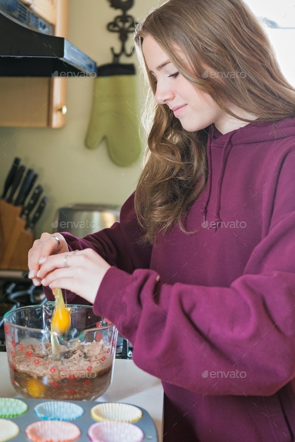 Teen girl cracking an egg into cake batter to bake cupcakes