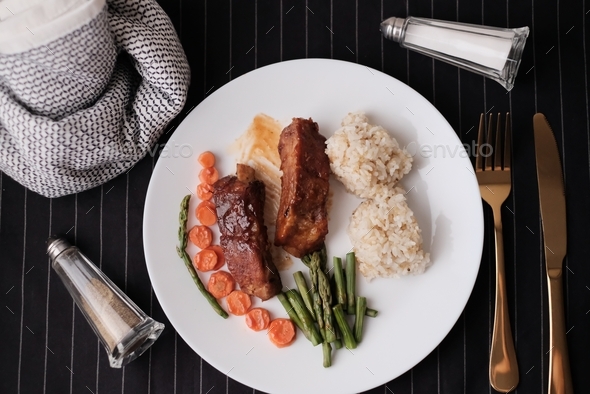  grilled rib on white plate with rice and asparagus on dark background with gold knife