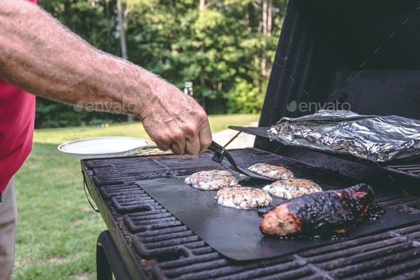 A man grills a pork tenderloin at home on an outdoor grill using a grill mat