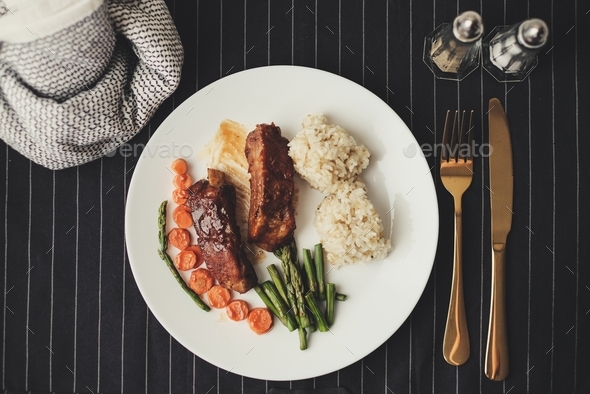  grilled rib on white plate with rice and asparagus on dark background with gold knife