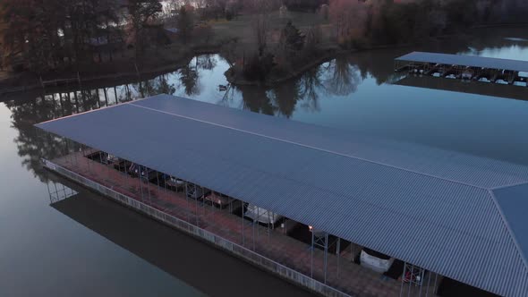 Aerial footage flying over boat docks towards land at sunset with reflections in the calm water alt