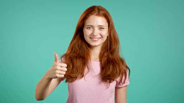 Young Woman Showing Thumb Up Sign Over Blue Background. Positive Young Girl Smiles To Camera. Winner alt