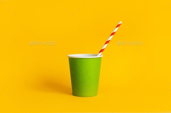 Green paper cup with striped paper straw on yellow background, biodegradable disposable tableware