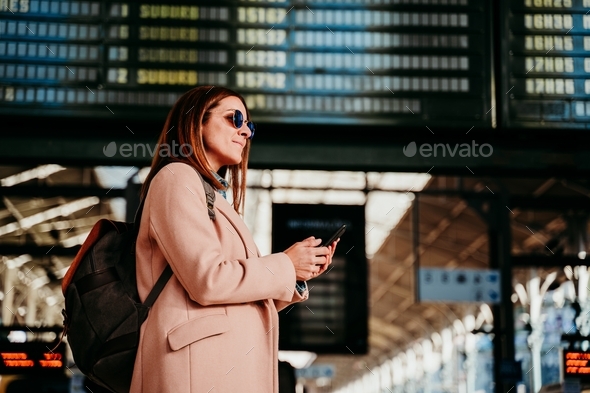 young woman at train station looking at destination board. Travel and public transport concept