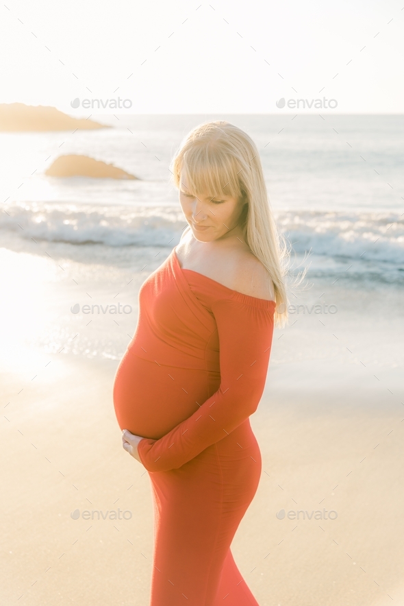 Blonde woman in red maternity dress on beach