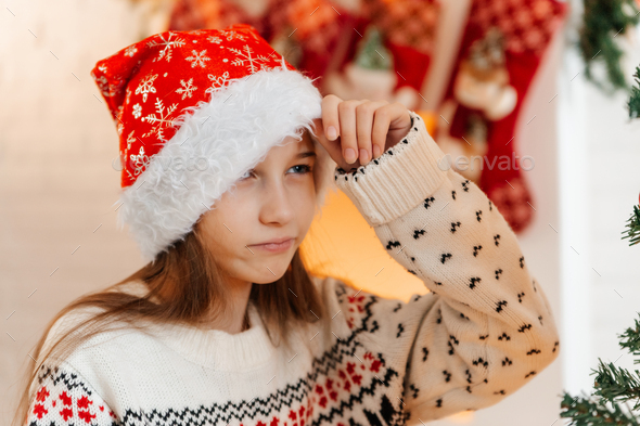 Portrait of a cheerful girl in a red Santa hat and a Christmas sweater - Stock Photo - Images