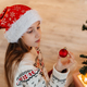 Girl in Santa hat smiling and hanging multi-coloured balls on Christmas tree - PhotoDune Item for Sale