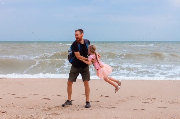 Father holds his cute daughter in arms, circles around himself, play and have fun together on sea.