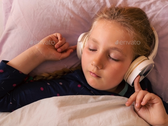 Blonde child girl in headphones listening to music for better sleep relaxing calming podcast
