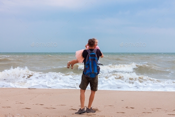 Father holds his cute daughter in arms, circles around himself, play and have fun together on sea