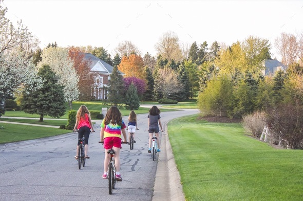 Four 4 teen girls biking in the suburbs through a neighborhood with trees changing colors