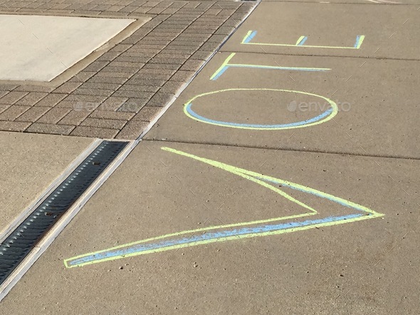 The word VOTE written with sidewalk chalk on cement as reminder for people to register & cast votes