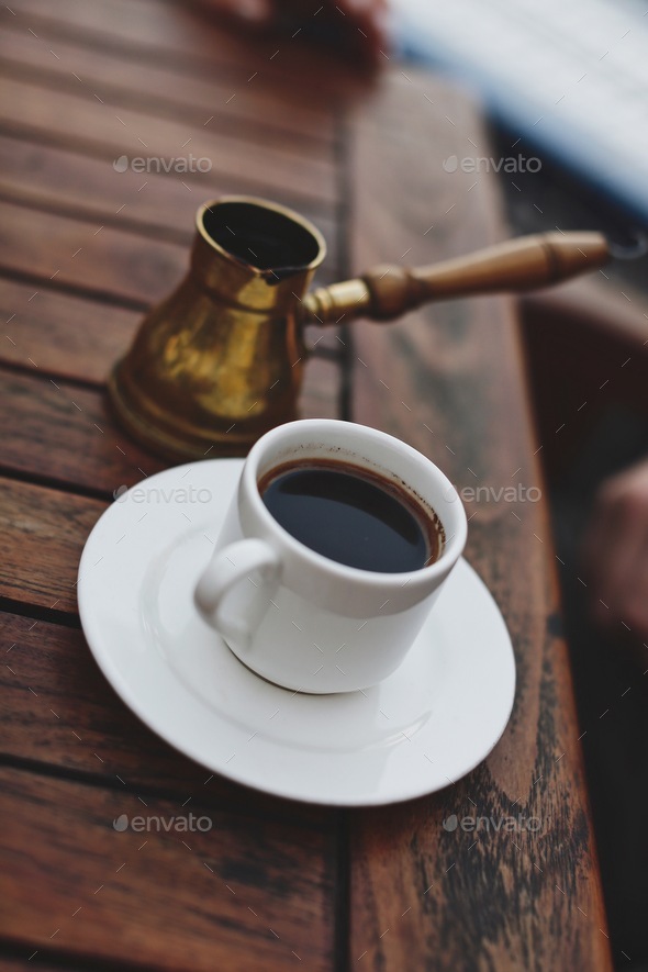 A cup of Turkish coffee, served from a copper cezve, in Turkey. White coffee cup on a wooden table.