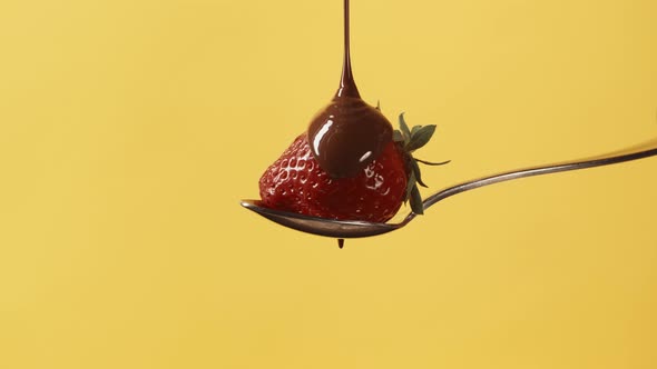 Fresh Strawberry on Metal Pastry Spoon Covering with Melted Liquid Chocolate on Yellow Background alt