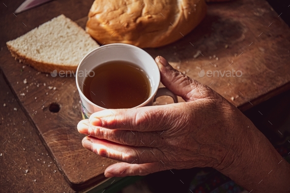 Elder wrinkled skin hand touch cup of tea in rustic scene