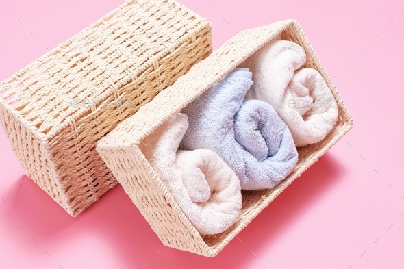 Folded towels in wicker boxes close-up on in pink background, space organization concept.