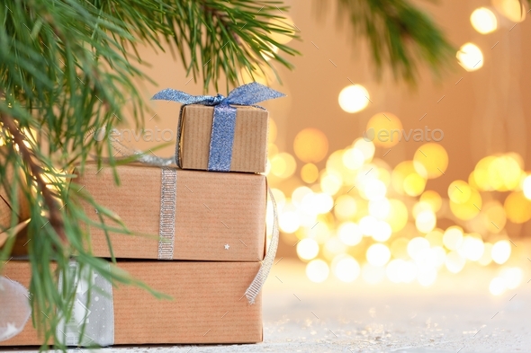 Stacks of Christmas gift boxes laid under a Christmas tree with defocused lights.