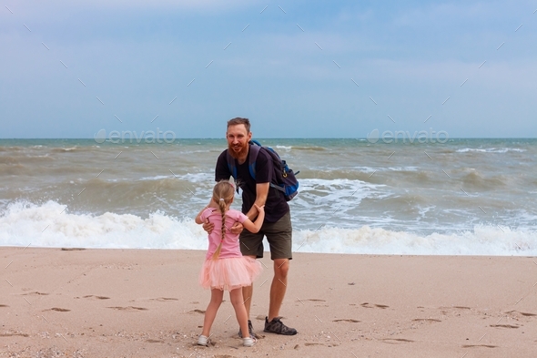 Father holds his cute daughter in arms, circles around himself, play and have fun together on sea