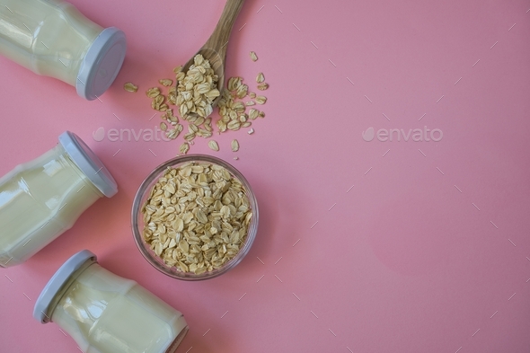 Oat flakes and oat drink in glass jars on pastel pink background. Healthy lifestyle and diet concept