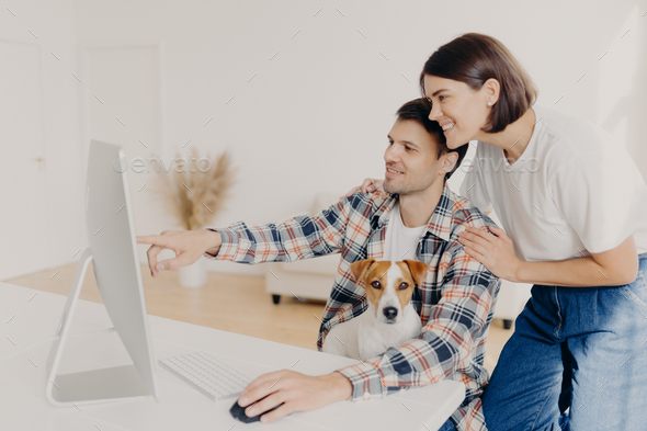 Happy husband points into monitor of computer, asks for useful advice in wife what better to buy,