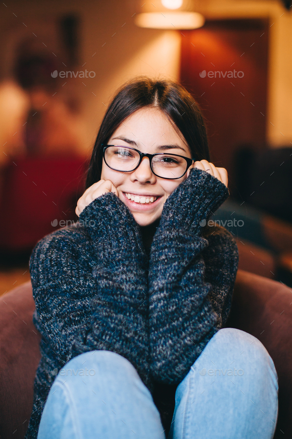 Shy teenage girl wearing eyewear sitting in cafe,smiling, relaxi