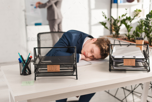 selective focus of document trays with lettering near businessman sleeping at desk near,