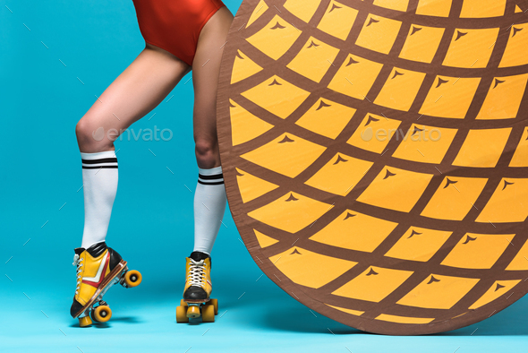cropped view of woman in knee socks and roller skates near decorative pineapple on blue