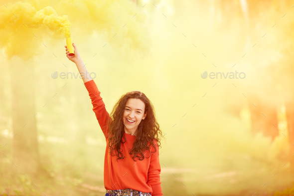 hipster girl in red clothes coloring sky with a smoke colored bomb