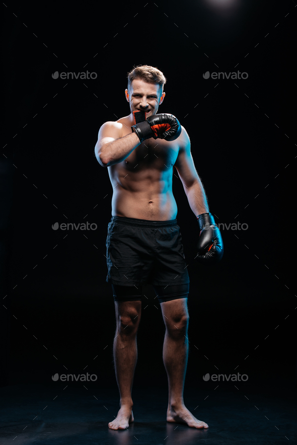 muscular barefoot sporty boxer taking off boxing gloves with mouth on ...