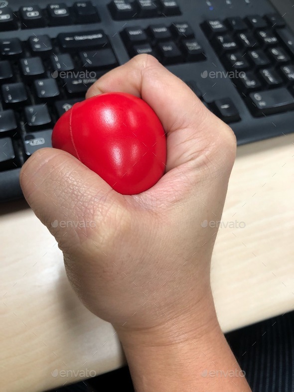 A hand squeezing a stress ball while at work in the office to manage emotional stress.