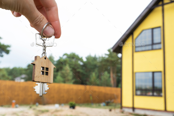 A hand with the keys to a new house on the background of an unfinished cottage