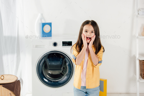 frightened child in yellow shirt and jeans standing in laundry room