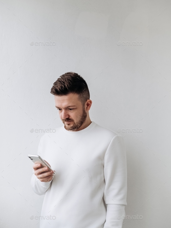 Young male getting bad news online by mobile phone. Scrolling social media feed