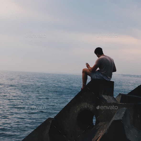 Guys sitting on rocks looking at the ocean and waves Stock Photo by ...