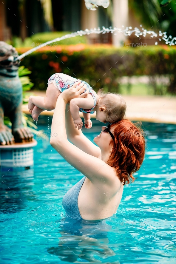 Middle aged caucasian mother and her infant daughter having fun in swimming pool in tropical country
