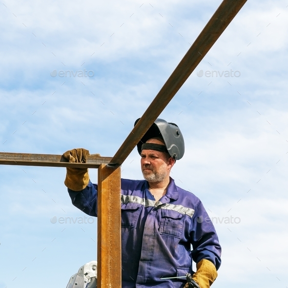 An industry worker is a builder, a male welder works at height in a protective welding mask