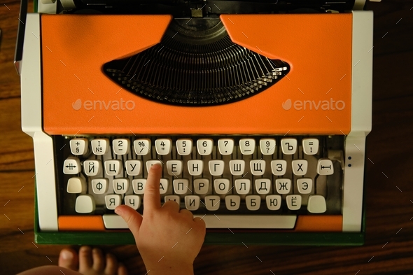 Children\'s hand presses Russian letter on orange vintage typewriter. Child learns letters