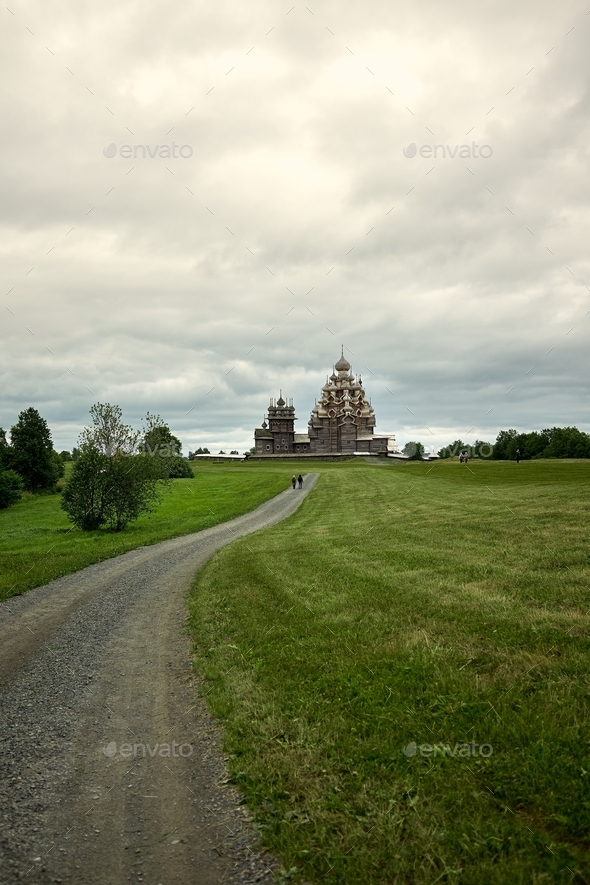 Gravel road leads through a field to a wooden Orthodox church on the island of Kizhi Karelia