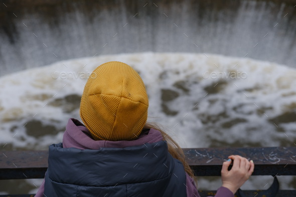 Girl watching the flow of water on the dam. Back view.