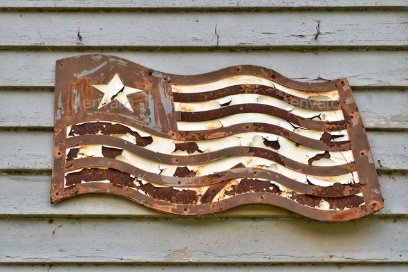 An old rusty metal American flag on grey wall of house. Patriotic decorations in rural Indiana, USA