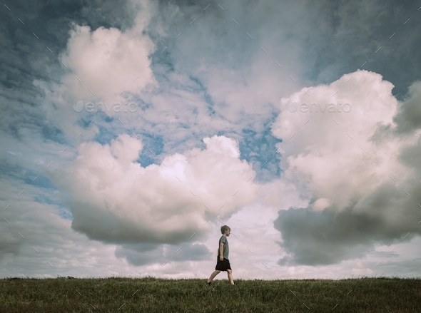 A boy walking across the top of a hill.  - Stock Photo - Images