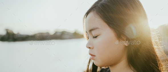 Preteen girl meditating with eyes closed by lake,child positive mental health,peace and hope concept