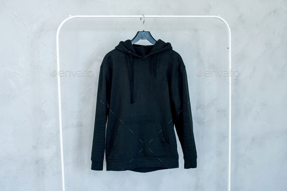Mock-up of a black hoodie,pocket, hanging on a hanger, holding in his hands, a sweatshirt with pleat