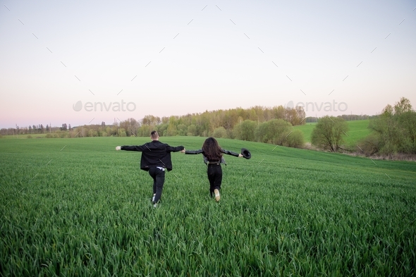 A guy and a girl are running in a green field with their arms outstretched
