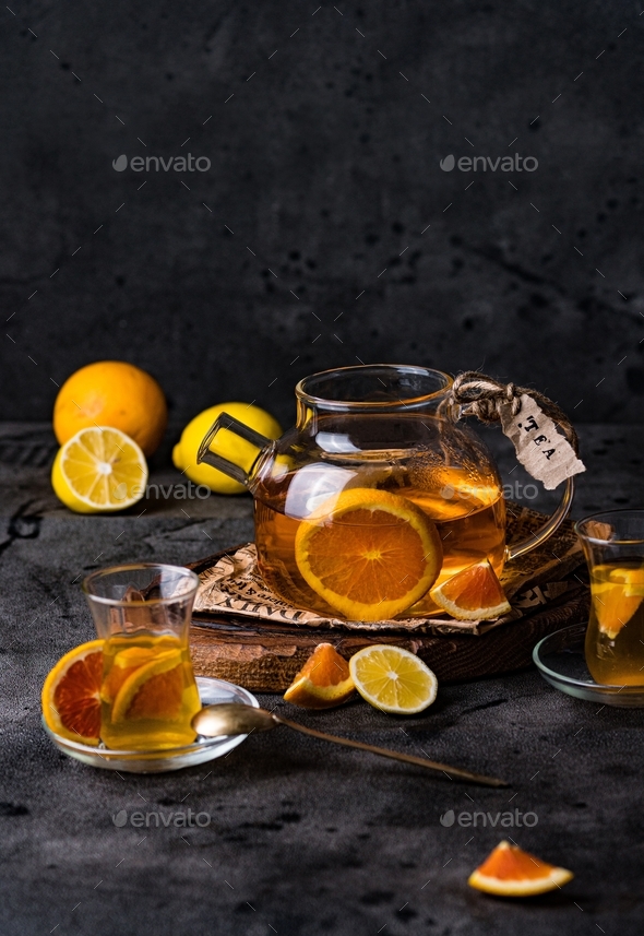 Lemon orange tea in a glass teapot with cups and citrus fruit slices. Stock Photo by alinanikitaeva