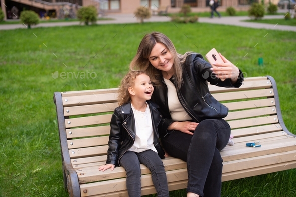 Charming mom holds the phone and takes a selfie with her daughter, the girl laughs