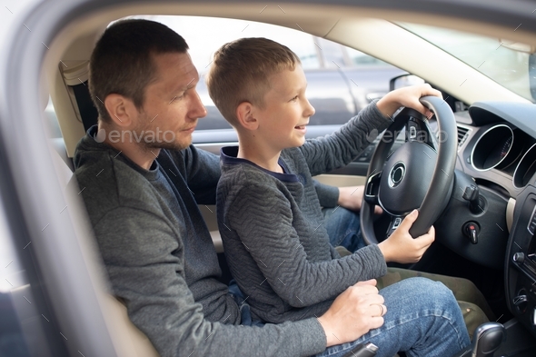 Dad and a cute boy hold the steering wheel of a car with their hands