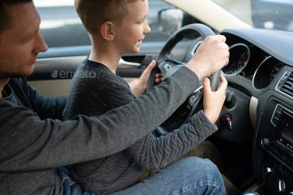 Dad and a cute boy hold the steering wheel of a car with their hands
